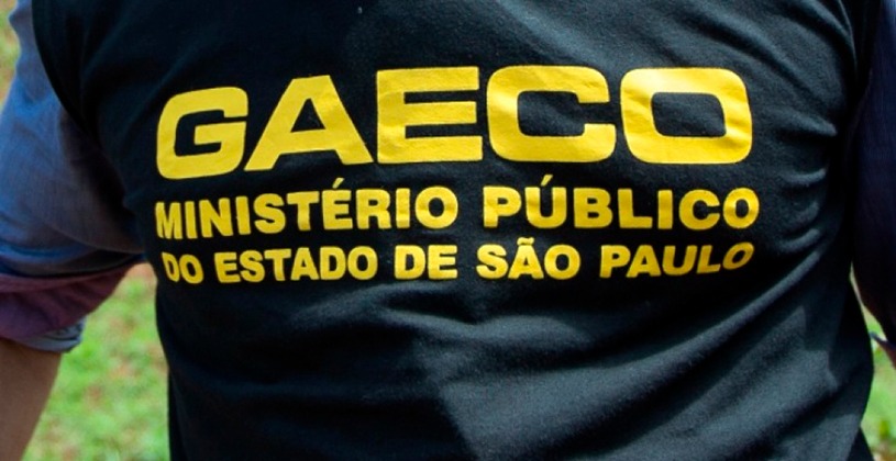 Imagem mostrando homem de costas usando colete preto com a inscrição GAECO